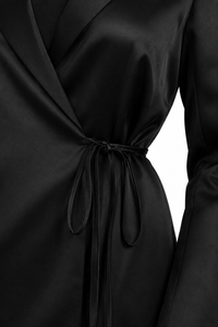Blouse tuxedo Carolina Herrera en satin noir de la collection Été 2024, style veste croisée avec revers en pointe, nœud latéral à la taille, fermeture boutonnée dissimulée, structure de blazer avec légèreté d'une blouse, fabriquée en Italie
_détail de la boucle