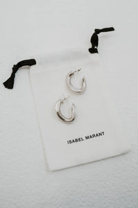 Boucles d'oreilles créoles Isabel Marant The Links en laiton plaqué argent, design de maillons entrelacés, silhouette semi-ouverte contemporaine, gravure signature Isabel Marant, fermeture à tige et poussoir, fabrication italienne avec sac