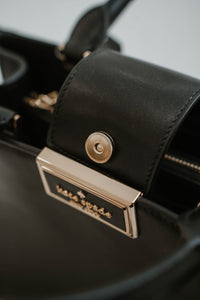 Sac cartable Kate Spade Reegan en cuir lisse noir, silhouette structurée, fermeture magnétique à rabat, logo signature sur quincaillerie, bandoulière 22 pouces, compartiment zippé central, poche arrière intérieure - Fermeture