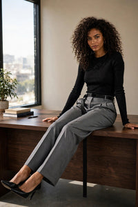 Pantalon Juanita Max Mara en laine grise chinée à ceinture noire, porté semi-assise sur un bureau en noyer, vue éditoriale lifestyle - PrettyInsideOut