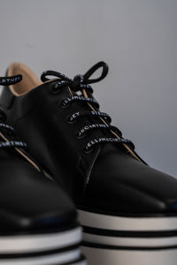 Baskets compensées Stella McCartney Sneak-Elyse en microfibre végane noire, semelle plateforme micro-dentée bicolore noir et blanc, bout carré anguleux, ruban rayé signature au talon, confection italienne_détail lacets